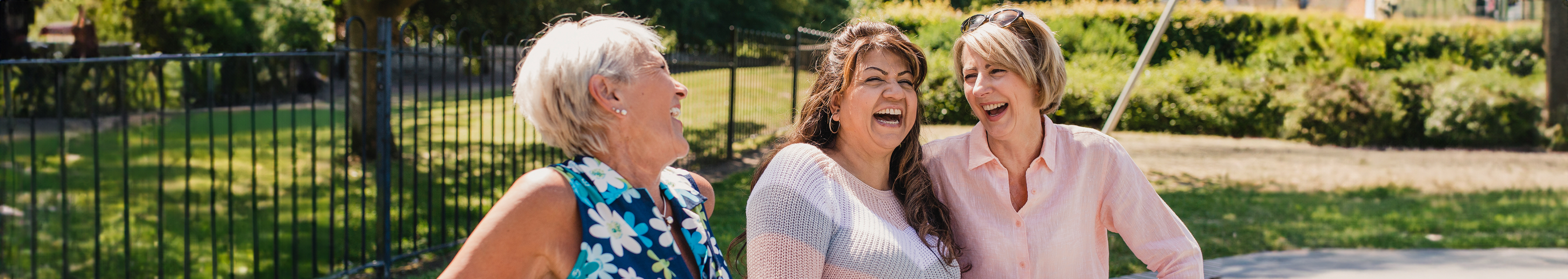 Three elderly women sitting in a park are laughing